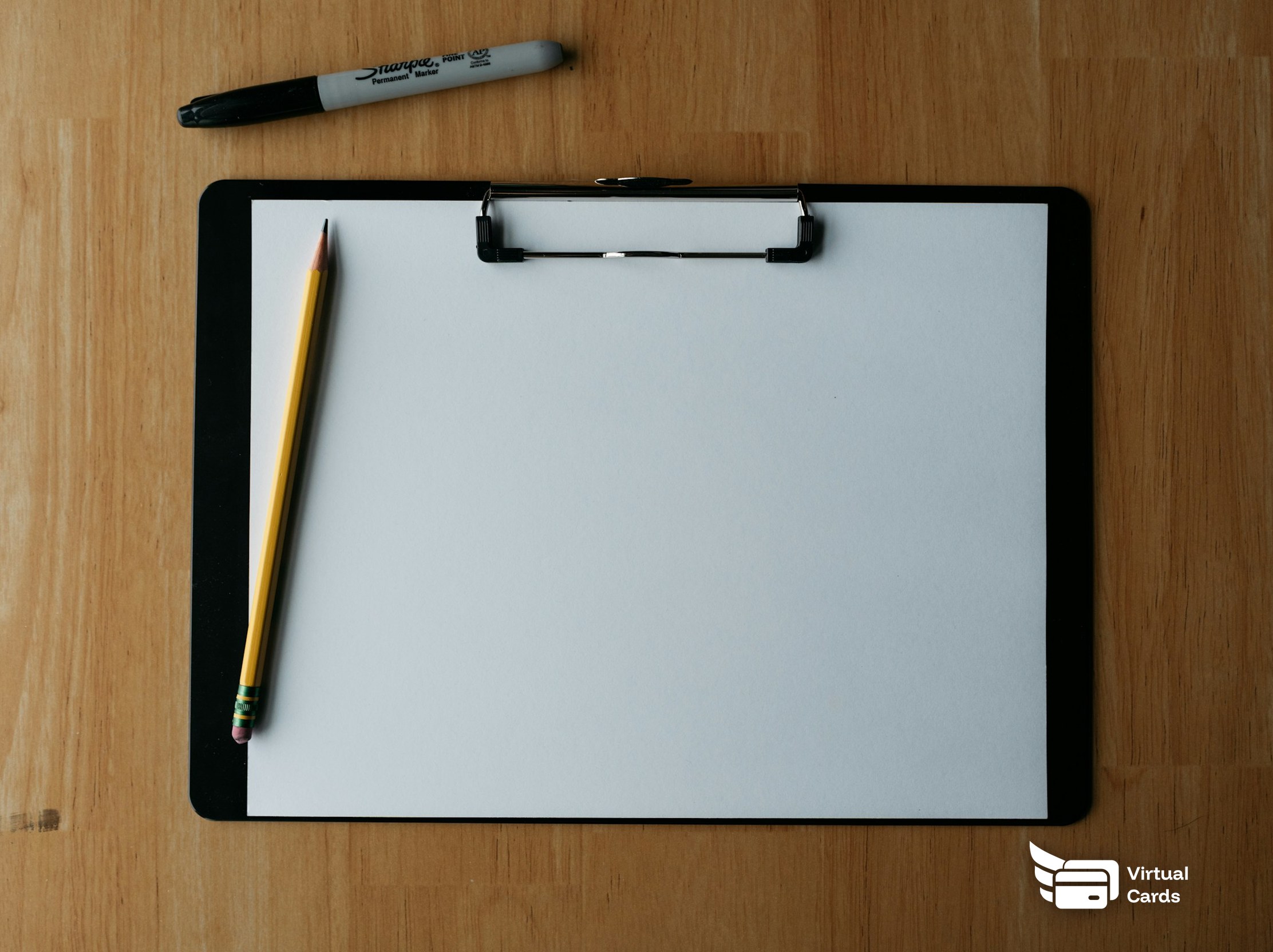 A clipboard with a pen and pencil resting on a wooden desk.