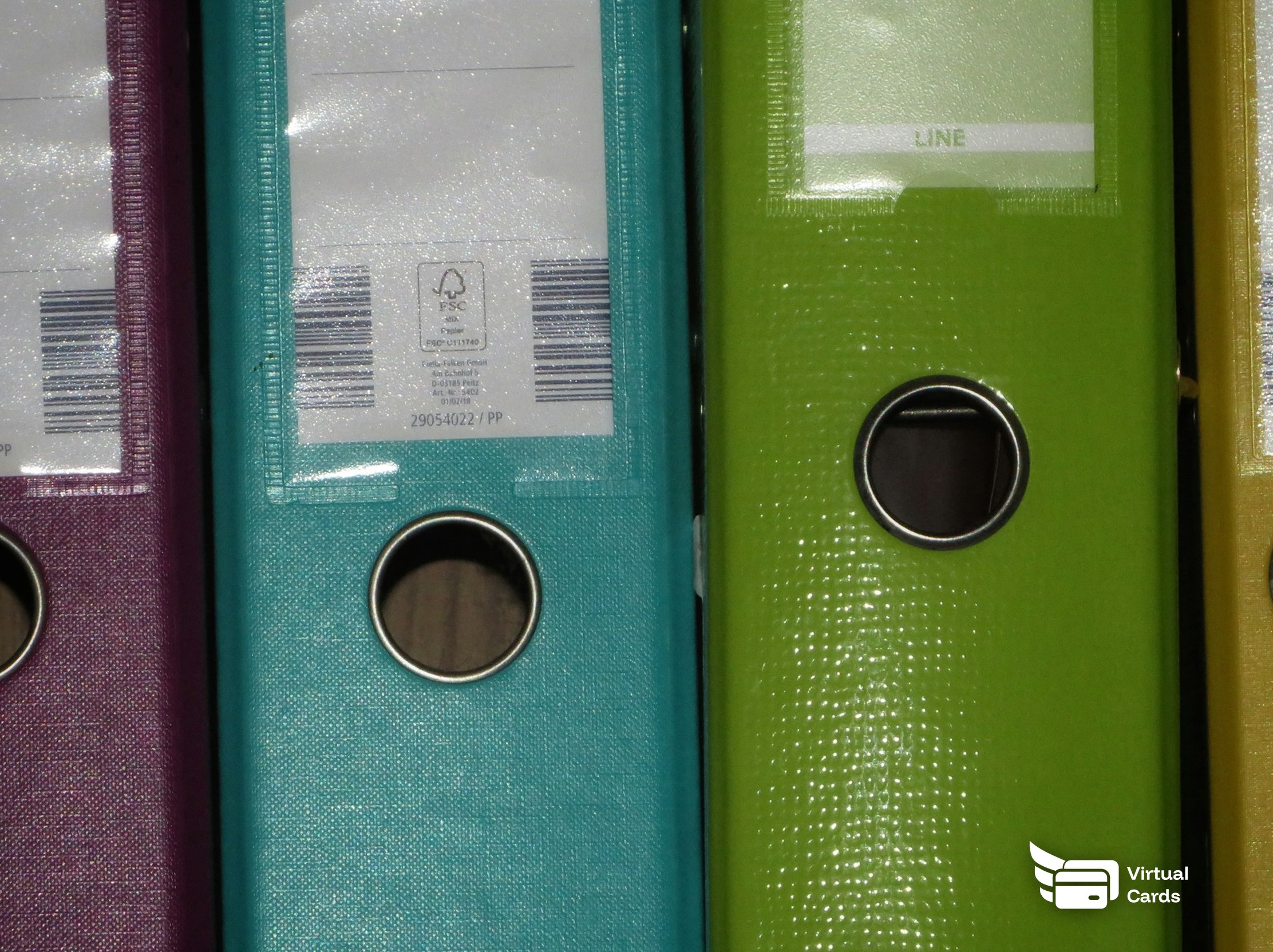 A row of colorful binders standing side by side, representing billable client expenses separated onto a capped virtual Visa card per client.