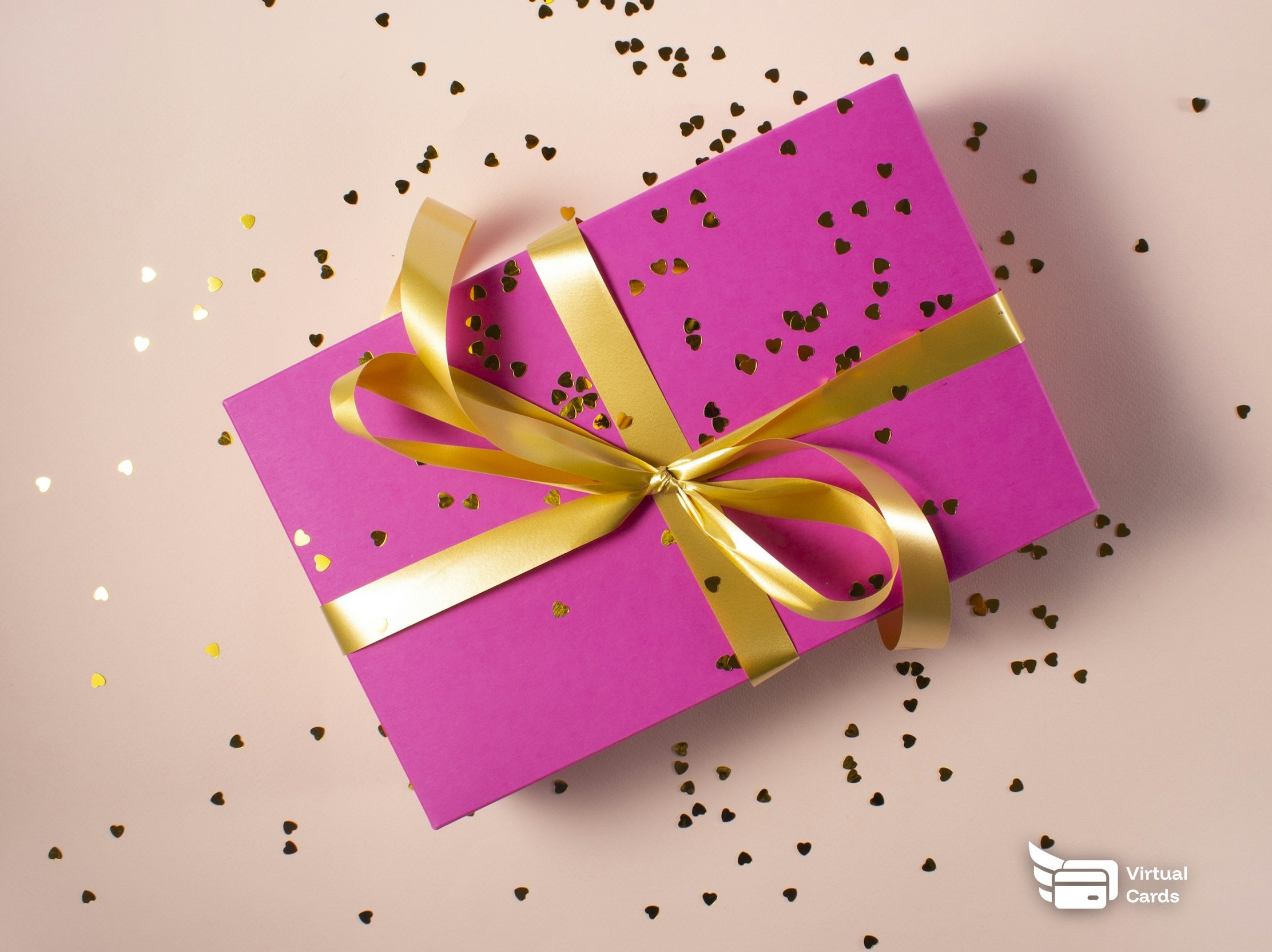 A pink gift box tied with a gold ribbon on a soft background.