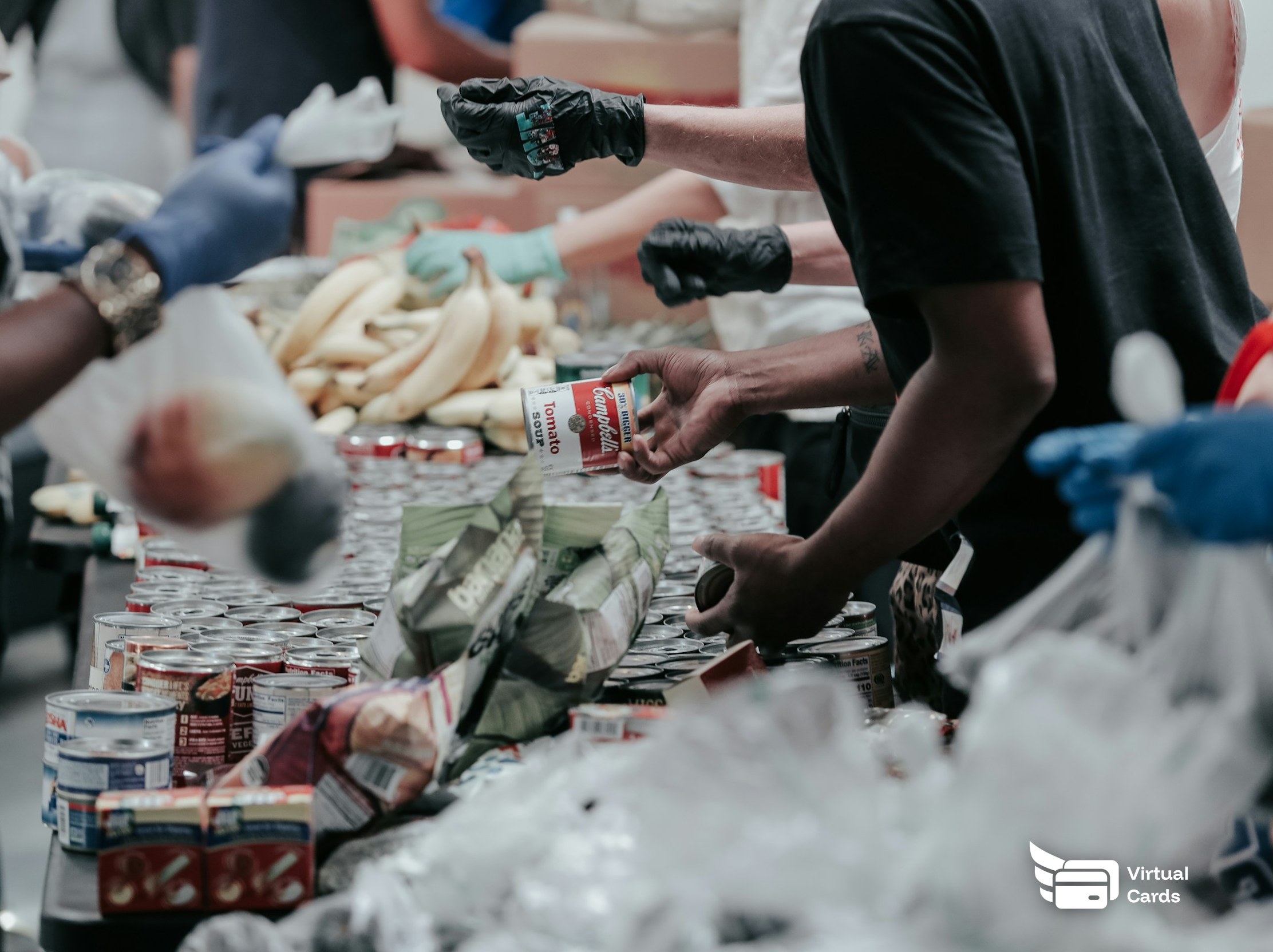 Volunteers in gloves sorting donated canned food at a community food bank, representing nonprofit and grant spending managed on capped virtual Visa cards.