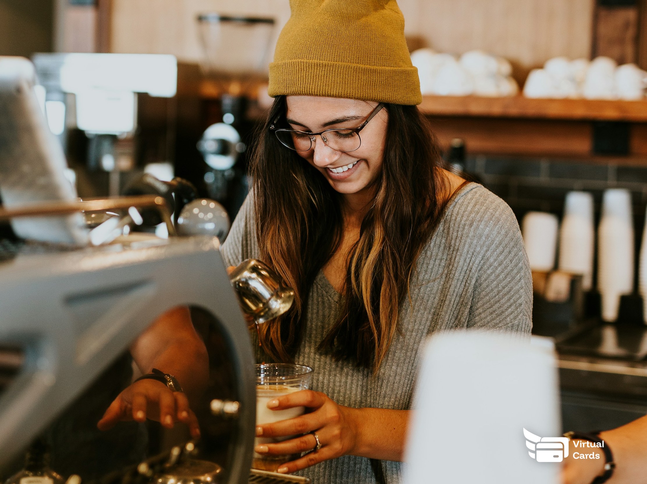 A smiling cafe worker making coffee behind the counter, representing paying staff without a bank account using a virtual Visa card.