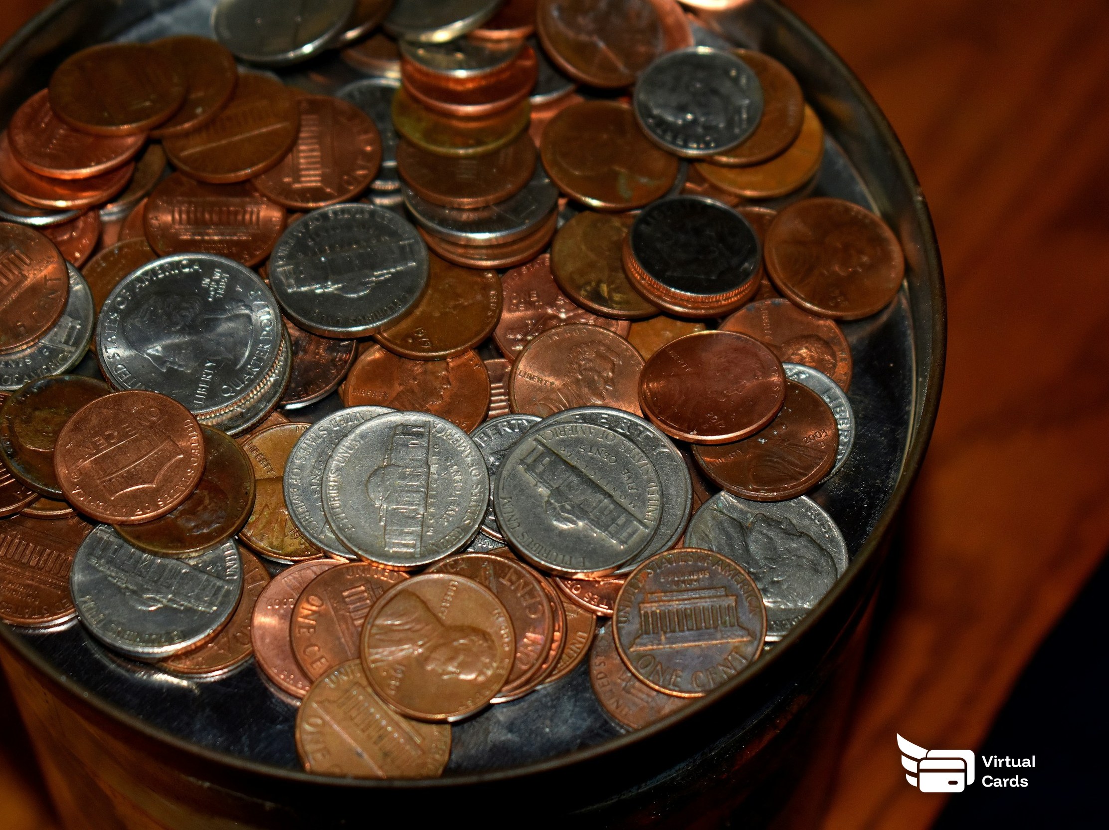 A metal tin filled with loose coins on a desk, representing replacing office petty cash with capped virtual Visa cards.