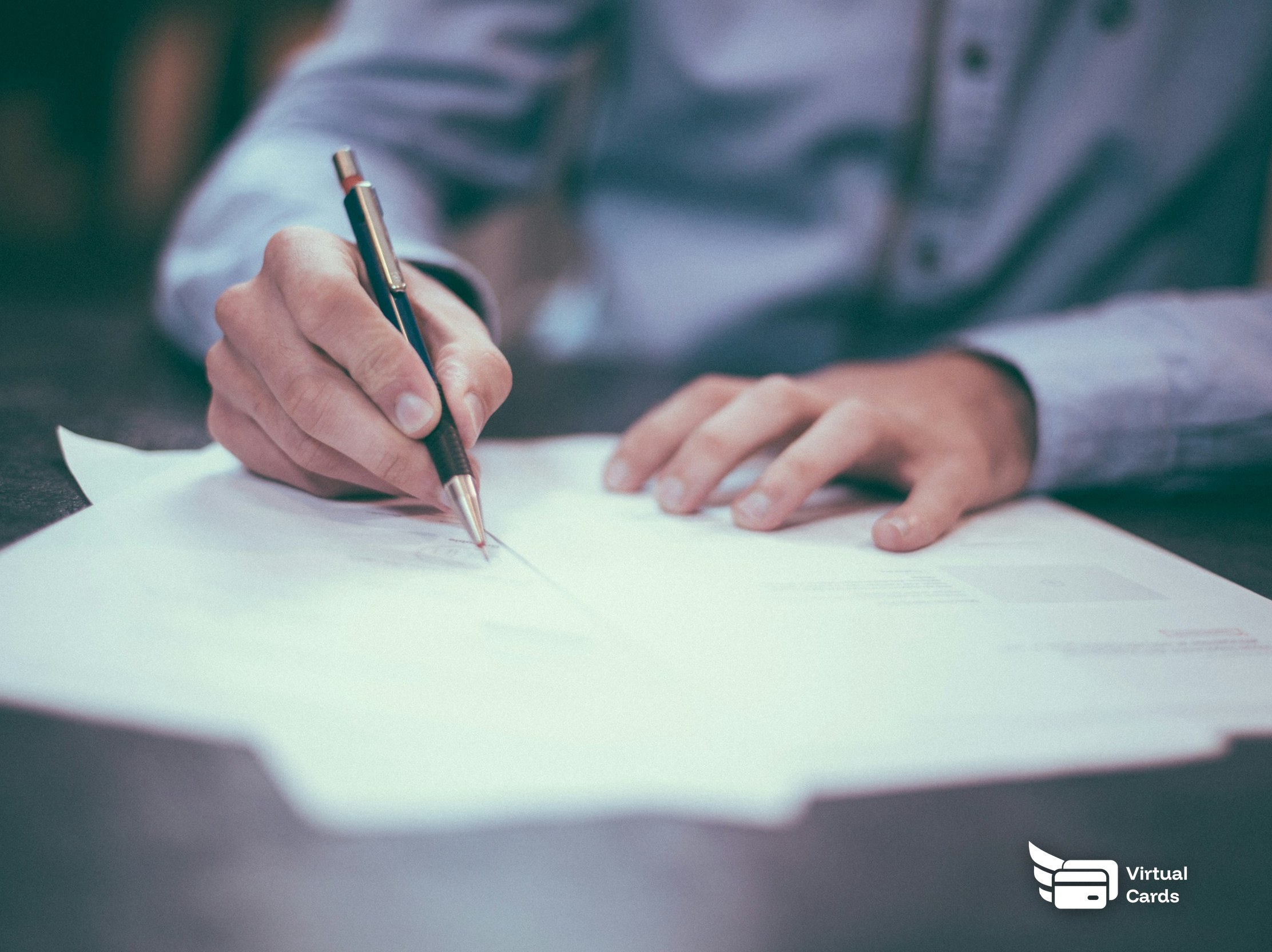 A person signing a financial document with a pen at a desk.