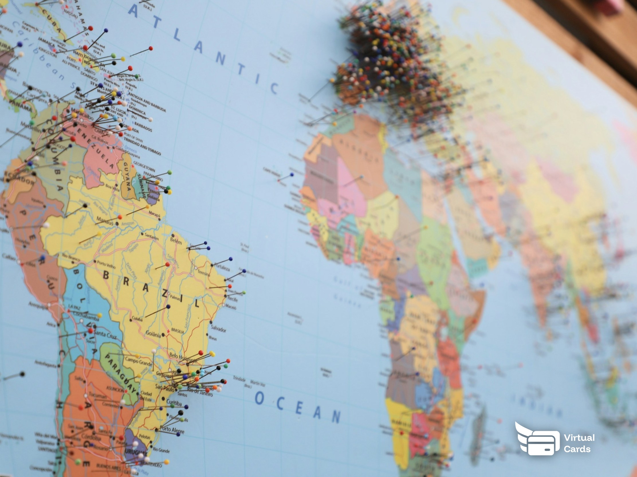 A large world map on a wall marked with colorful push pins, representing a distributed remote team each carrying their own capped virtual Visa spending card.