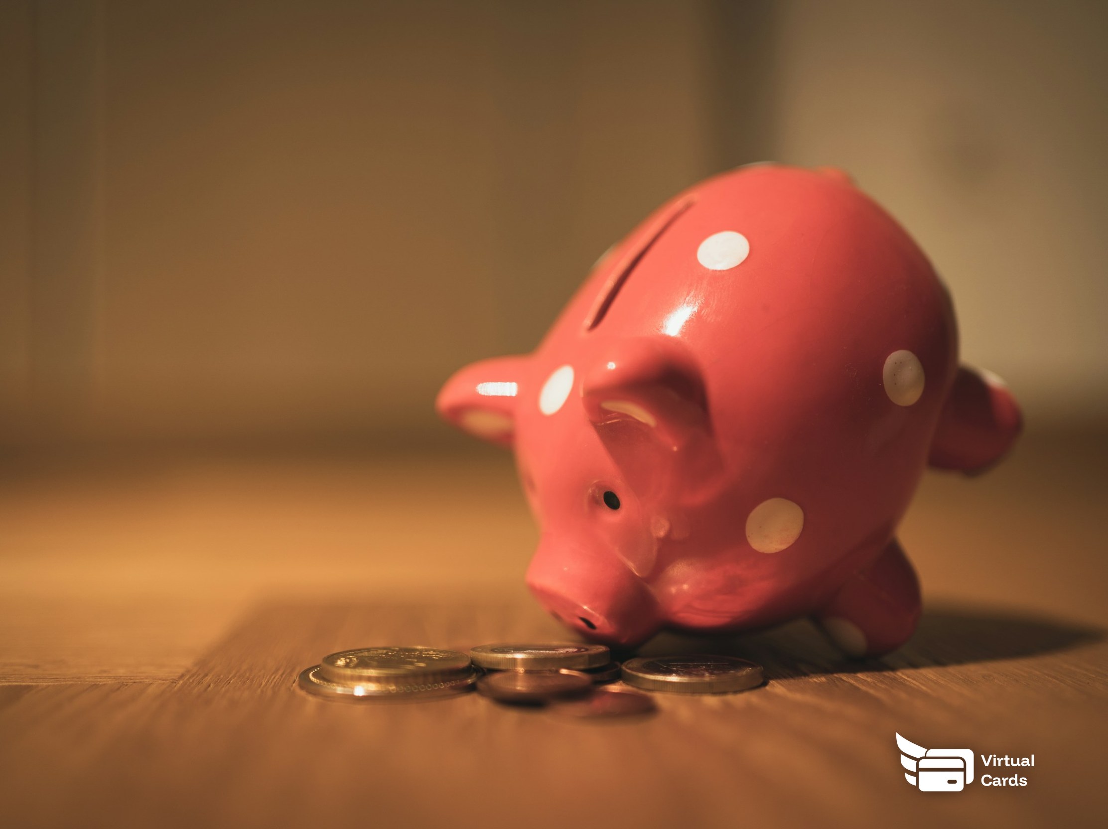 A pink piggy bank beside a small stack of coins on a table.