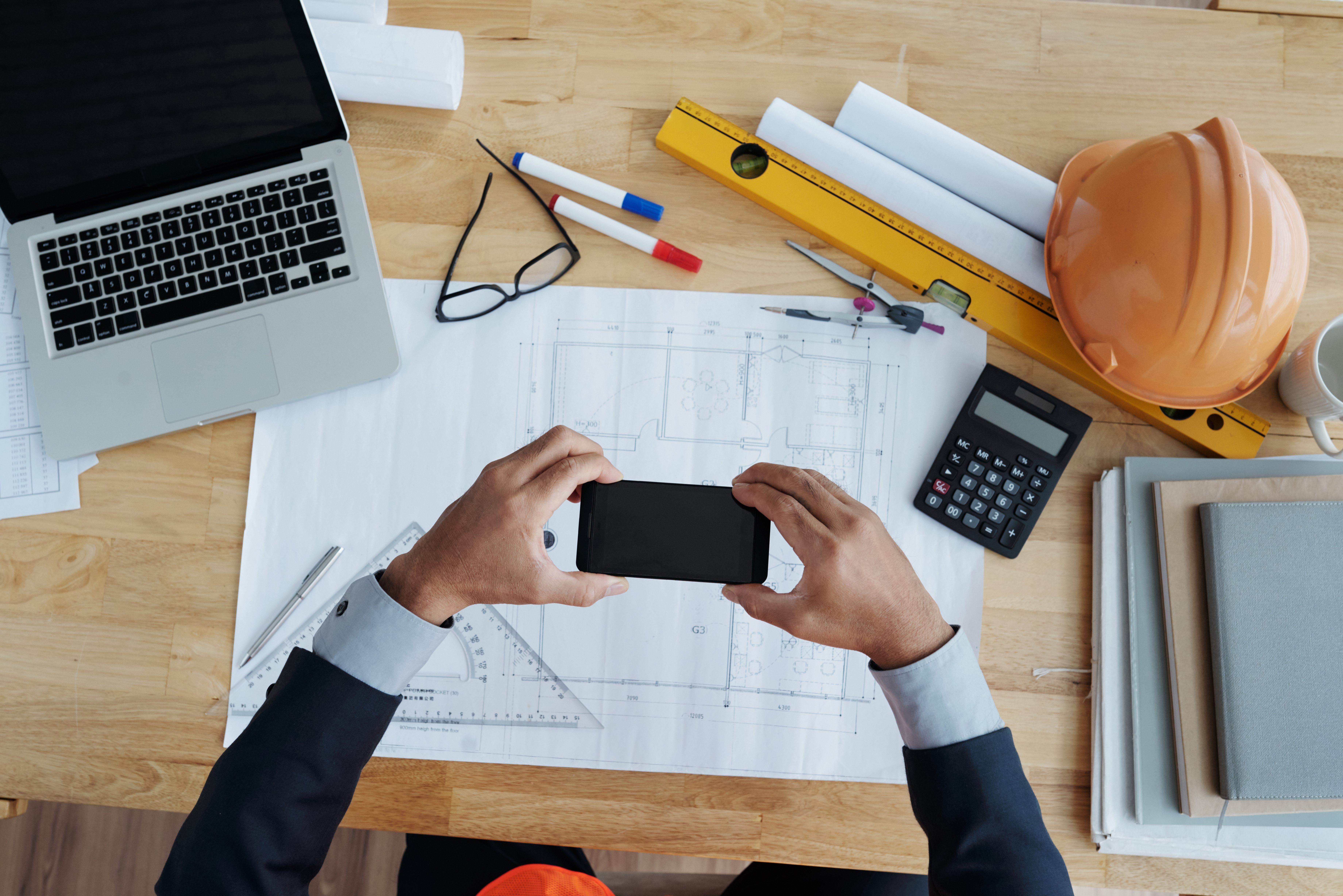 Construction manager checking job costs on a smartphone over a blueprint