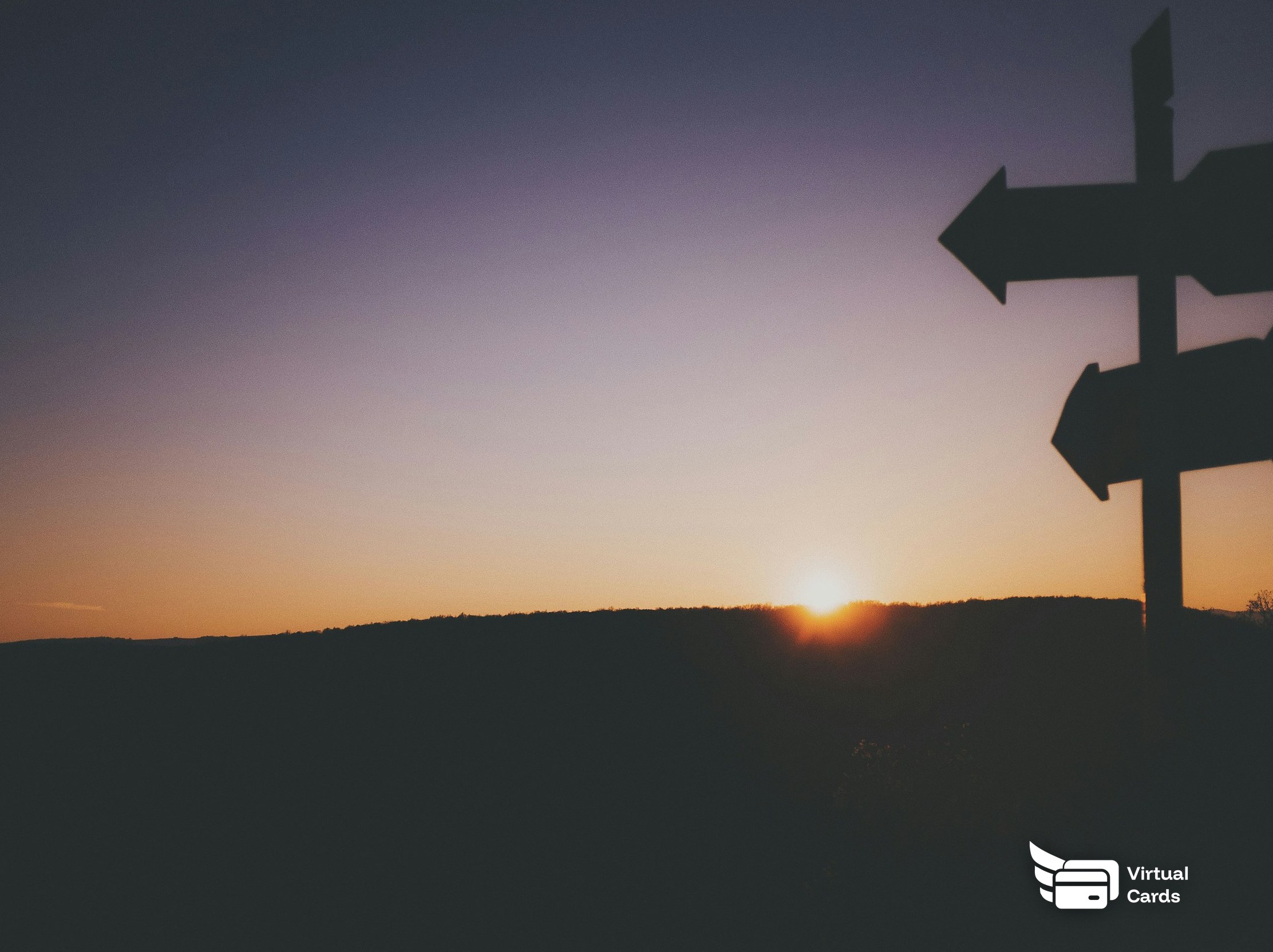 A wooden signpost with two arrows pointing different ways at sunset.